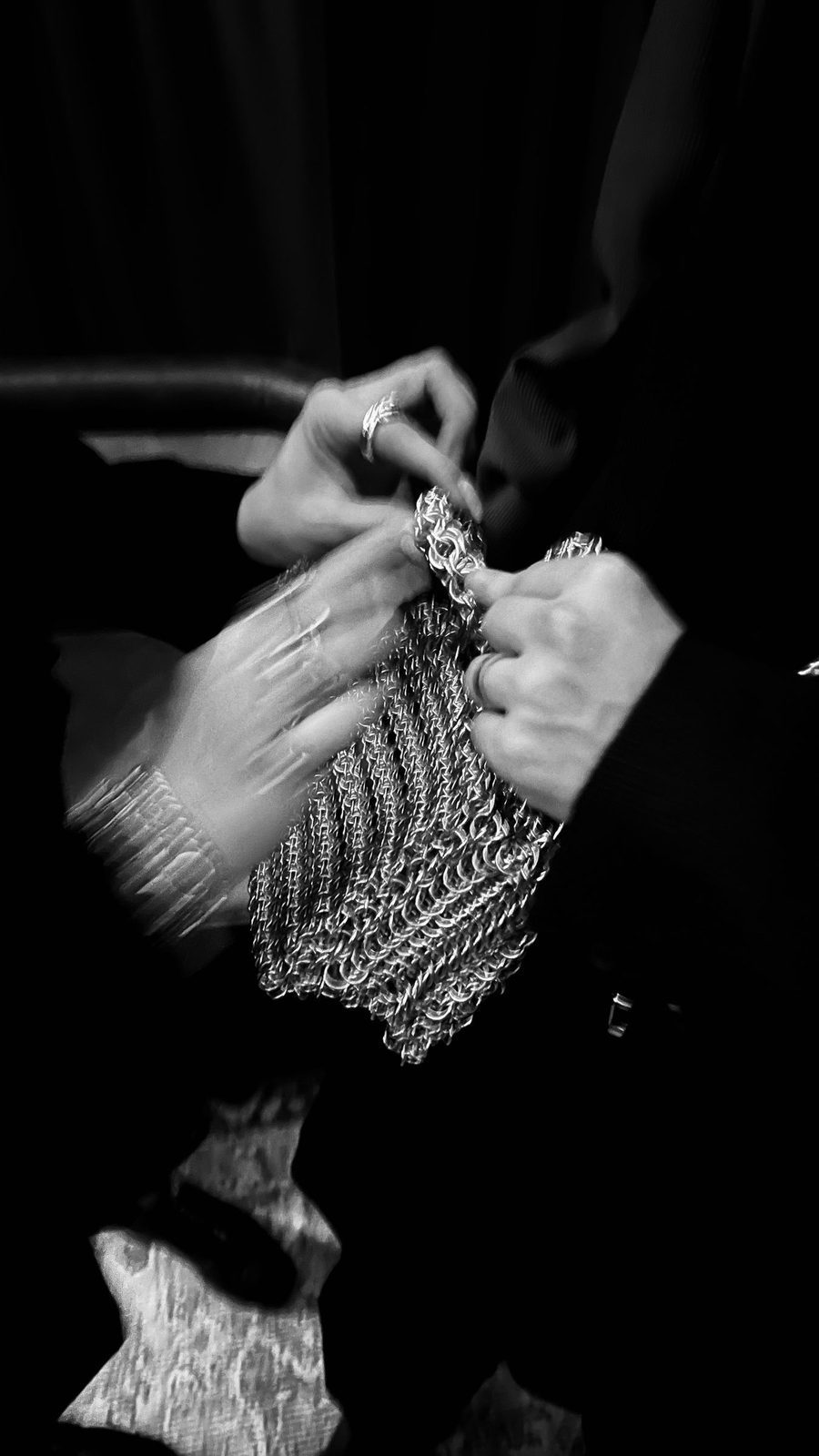 Black and white close-up of two hands holding the Free Maison Nowy Chainmail Bag at the Free Maison pop-up event with FERN at a speakeasy NYC deli, where guests were invited to experience the brand in an intimate setting. The individual interlocked aluminum rings of classical maille construction are visible in fine detail.