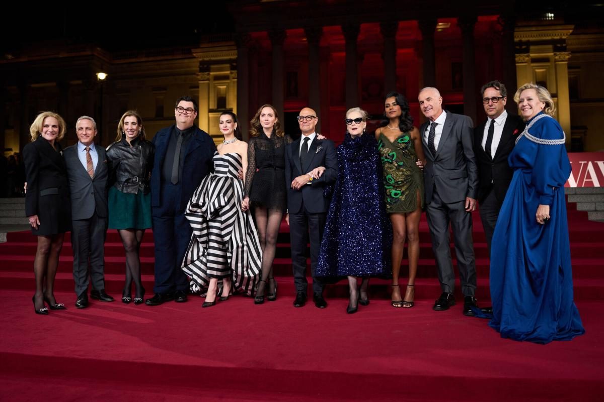 The full cast and crew of The Devil Wears Prada 2 on the red carpet at the London world premiere, including Anne Hathaway, Meryl Streep, Stanley Tucci, Emily Blunt, and the film's producers and director. Costume designer Molly Rogers stands among the group wearing a teal silk gown and the Free Maison Valenciennes Harness in silver hand-woven chainmail.