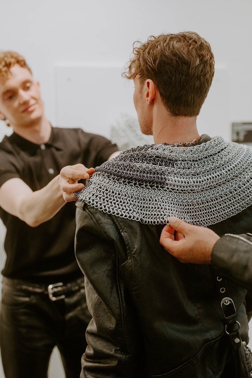 Free Maison co-founder Jesse Aviv fitting Gottmik with a custom Free Maison Hanover Silver Mane at the Free Maison New York Fashion Week 2024 opening. Gottmik stands still as Jesse carefully drapes and adjusts the hand-woven silver chainmail piece across their shoulders in the gallery space.