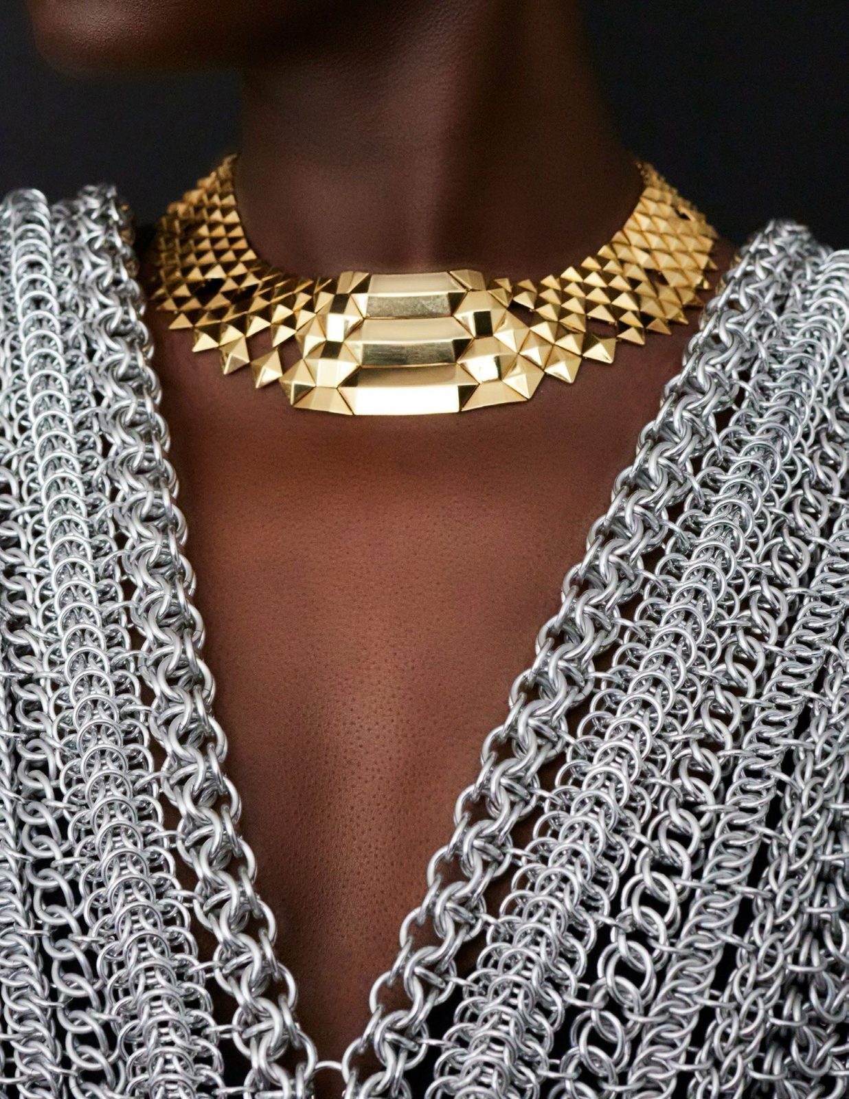 Accessories Council first jewelry edition shoot — a close-up of the Free Maison Aluminum Apega chainmail piece showing the proprietary ciphered technique in fine detail. Individual interlocked anodized aluminum rings are visible at the neck and collarbone, with gold and silver tones contrasting against a dark studio background.